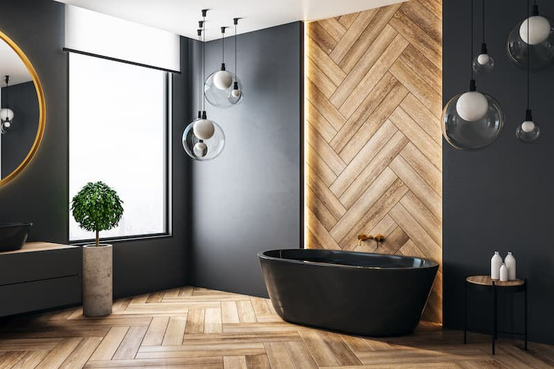 Blick auf ein schwarzes Bad. Hinter einer schwarzen, freistehenden Badewanne ist ein Teil der Wand mit Holzfliesen bedeckt, welche im Fischgrätenmuster angeordnet sind.