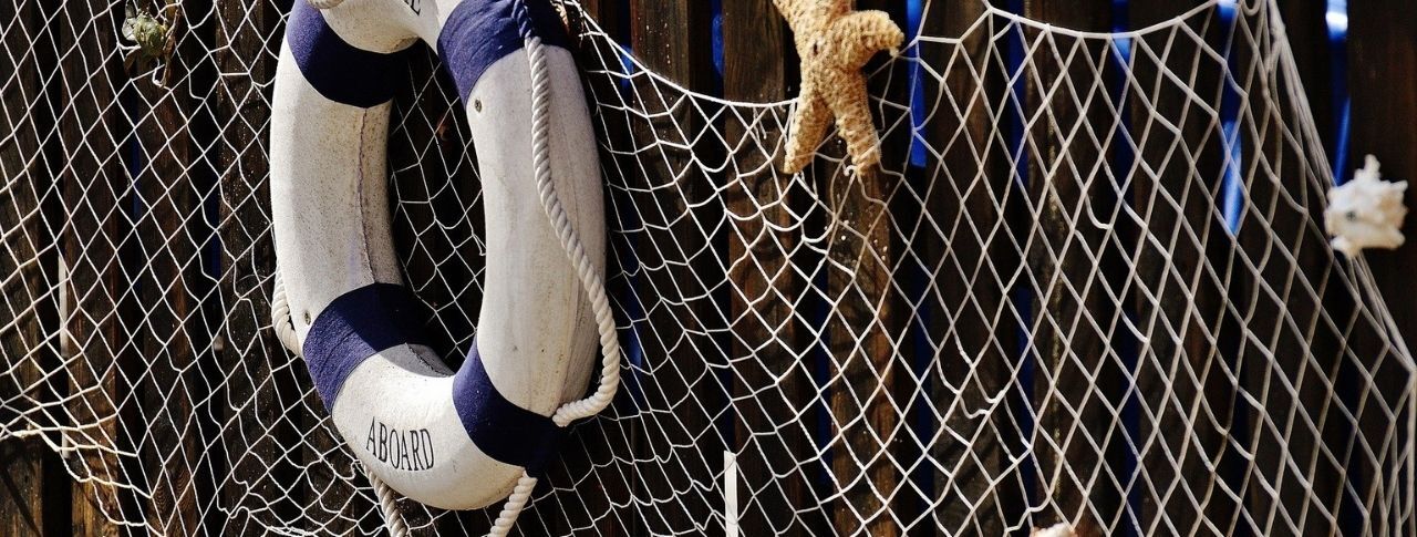 An einem aufgehängten Fischernetz hängen ein blau-weißer Rettungsring mit der Aufschrift 