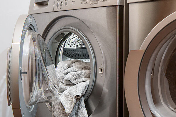 Beige Handtücher in der Trommel einer grauen Waschmaschine.